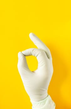 Hand in rubber glove. OK sign on bright yellow background