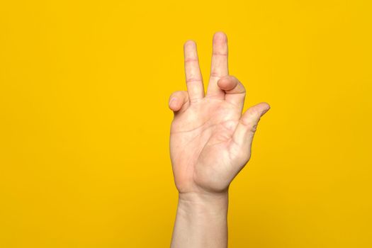 Tough man's hand making a strange and complicated gesture with his hand. It can represent a surfer, gippie or meditation gesture isolated on yellow background