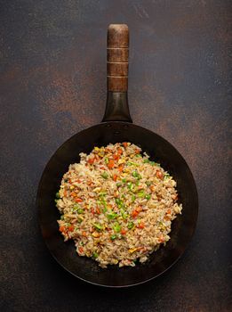Authentic Chinese and Asian fried rice with egg and vegetables in wok top view on rustic concrete table background. Traditional dish of China