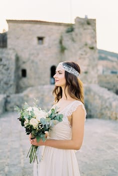 Bride with a bouquet of flowers in her hands against the backdrop of an old stone fortress. High quality photo