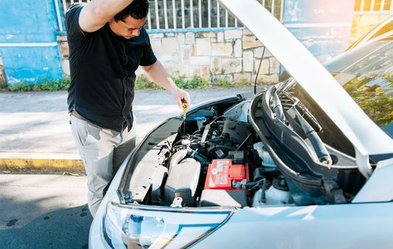 Man checking the oil in his vehicle. Person checking the oil level of his car in the street. Driver inspecting car oil level
