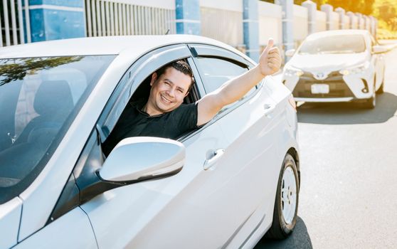 Smiling driver giving a thumbs up on the road. Satisfied driver man showing thumb up, safe driving concept. Young driver man in the car showing thumb up