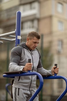 Athletic handsome man doing hanging leg raise at outdoor sports ground