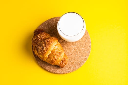 Breakfast bread and cup of milk on yellow and blue background