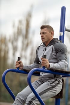 Athletic handsome man doing hanging leg raise at outdoor sports ground