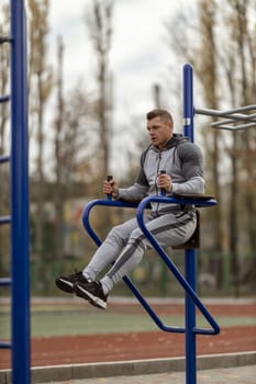 Athletic handsome man doing hanging leg raise at outdoor sports ground