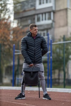 Athletic man in outerwear sportswear with a backpack posing on the sports ground outdoors