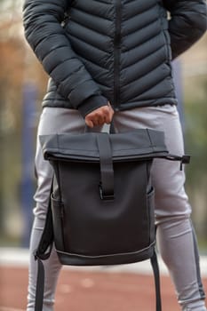 Man's hand holding a black sports backpack outdoors