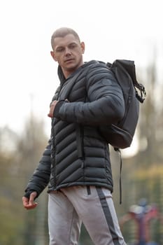 Athletic man in outerwear sportswear with a backpack posing on the sports ground outdoors