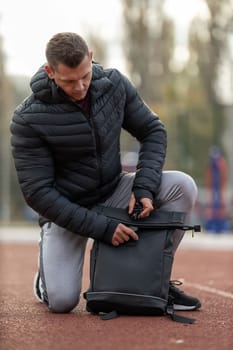 Athletic man in outerwear sportswear with a backpack posing on the sports ground outdoors