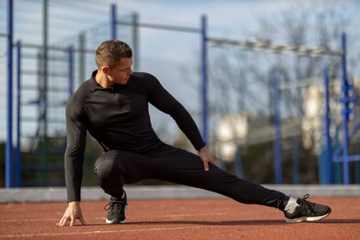 Male runner doing stretching exercises, getting ready for morning workout at outdoor sports ground