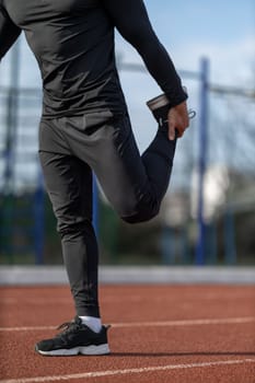 Male runner without face doing stretching exercises, getting ready for morning workout at outdoor sports ground