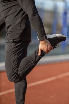 Male runner without face doing stretching exercises, getting ready for morning workout at outdoor sports ground