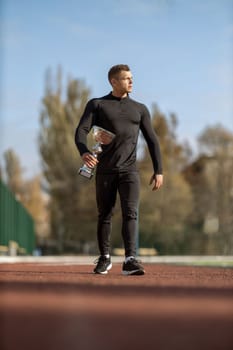Athletic man in black sportswear at football stadium with champion cup