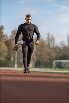 Athletic man in black sportswear at football stadium with champion cup