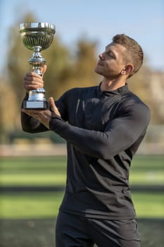 Athletic man in black sportswear at football stadium with champion cup