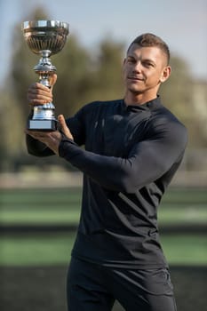 Athletic man in black sportswear at football stadium with champion cup