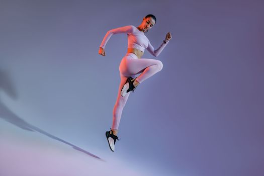 Athletic active woman jumping on studio background with colored filter. Dynamic movement