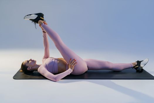 Athletic woman in sportswear doing stretching exercises on yoga mat on studio background