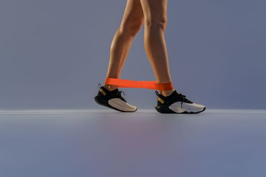 Close up of woman trains legs with fitness elastic band on studio background. High quality photo