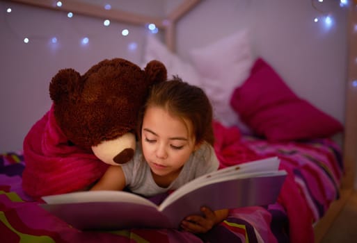 Its a story to spark the sweetest of dreams. a little girl reading a book in bed with her teddybear