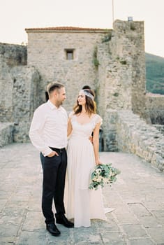 Bride and groom stand embracing on the bridge near the ruins of the old fortress. High quality photo