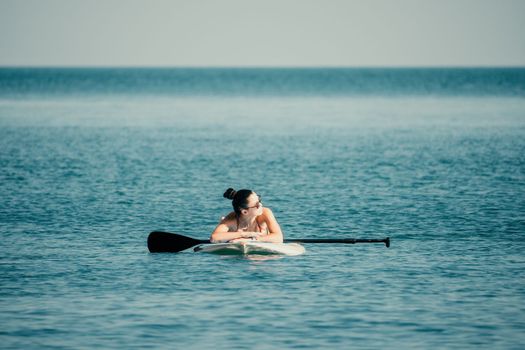 Sea woman sup. Silhouette of happy middle aged woman in rainbow bikini, surfing on SUP board, confident paddling through water surface. Idyllic sunset. Active lifestyle at sea or river