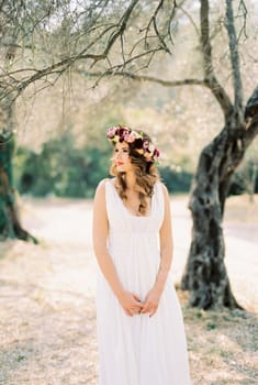 Bride in a toga dress with a wreath stands under a tree in the park. High quality photo