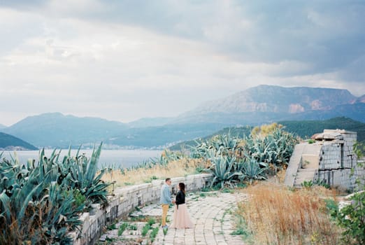 Bride and groom are standing on the ruins of a stone round platform near the agave bushes. High quality photo