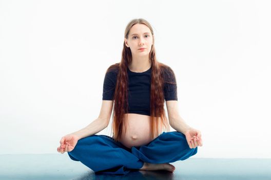 Pleasant pregnant woman posing in profile and trying yoga Young happy expectant relaxing, thinking about her baby and enjoying her future life. Motherhood, pregnancy, yoga concept, lotus position.