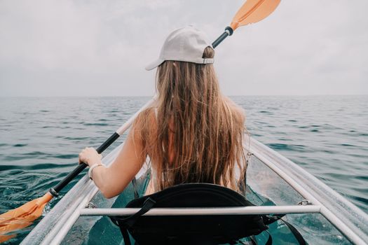 Woman in kayak back view. Happy young woman with long hair floating in transparent kayak on the crystal clear sea. Summer holiday vacation and cheerful female people having fun on the boat.