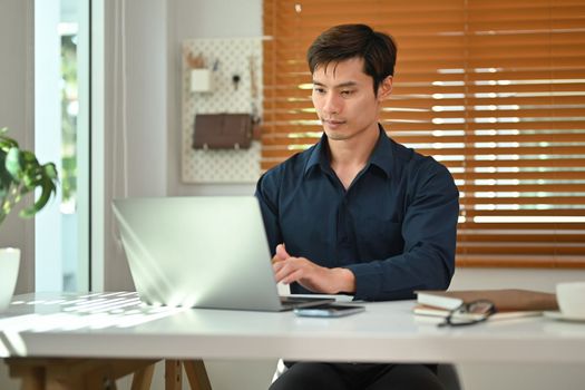 Handsome businessman using laptop computer working at home office. Remote job, technology and lifestyle concept.