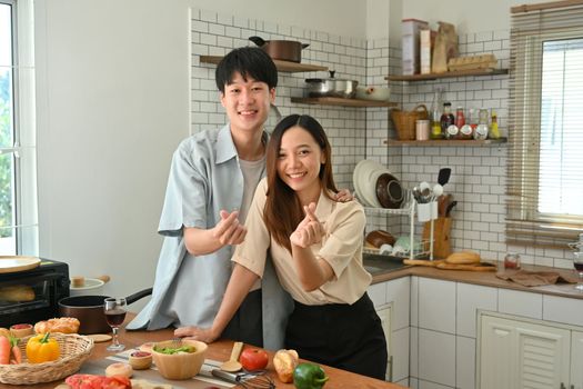 Image of married young couple showing heart with fingers gesture mini love and smiling to camera.