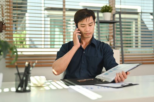 Attractive asian man having phone conversation while working remotely from home.