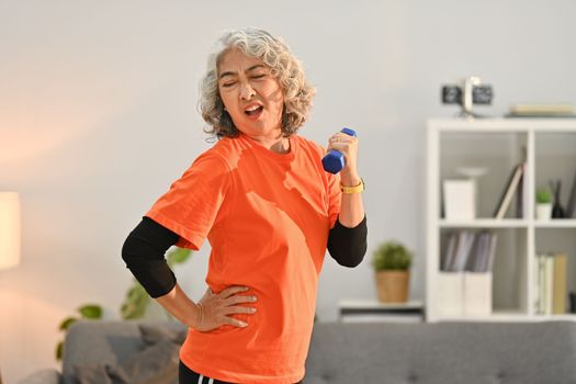 Active middle aged woman in sport clothes exercising with dumbbells in living room. Healthy active lifestyle concept.