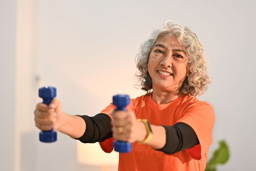 Active middle aged woman womanexercising with dumbbells at home. Retirement, healthy lifestyle concept.