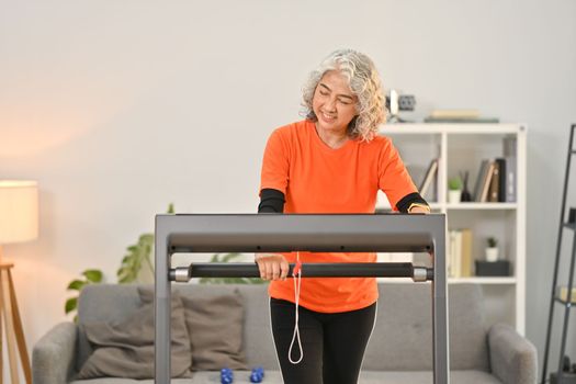 Smiling middle aged woman in sport clothes walking on treadmills in the morning at home. Healthy lifestyle concept.