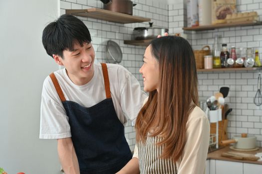 Cheerful asian man and wife having fun together in kitchen, enjoying spending free weekend time together at home.