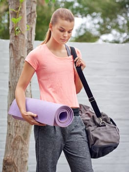 On her way to yoga class. a beautiful young woman carrying a yoga mat and bag