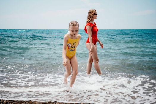 Happy loving family mother and daughter having fun together on the beach. Mum playing with her kid in holiday vacation next to the ocean - Family lifestyle and love concept.