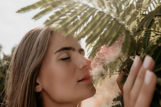 Beauty portrait of young woman closeup. Young girl smelling Chinese acacia pink blossoming flowers. Portrait of young woman in blooming spring, summer garden. Romantic vibe. Female and nature.