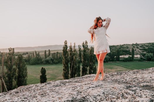 Romantic beautiful bride in white dress posing with sea and mountains in background. Stylish bride standing back on beautiful landscape of sea and mountains on sunset