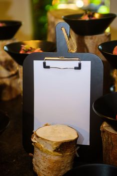 black clipboard with a white paper where you can write on in front of a defocused buffet