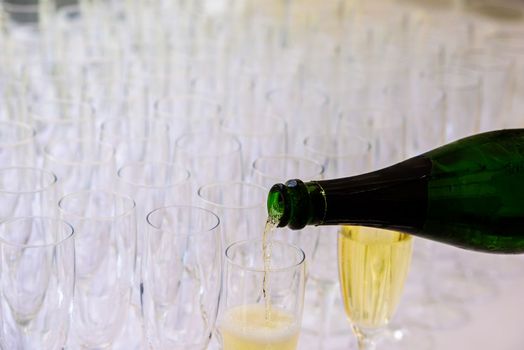 closeup of a champagne bottle pooring champagne into a champagne flute against a blurred glasses in the background