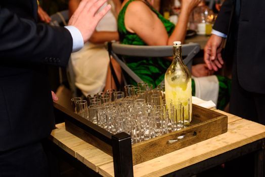 close-up of a waiter serving limoncello in glasses with a little wooden table at a party