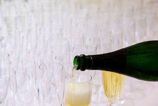 closeup of a champagne bottle pooring champagne into a champagne flute against a blurred glasses in the background