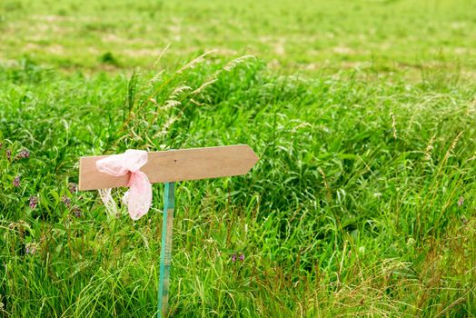 wooden arrow, where you can put text on with pink ribbon against a defocussed grassland with wild flowers