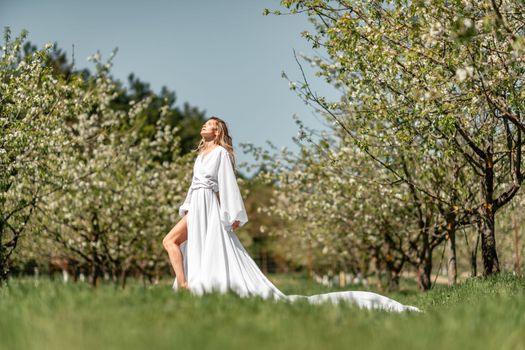 Blond blooming garden. A woman in a white dress walks through a blossoming cherry orchard. Long dress flies to the sides