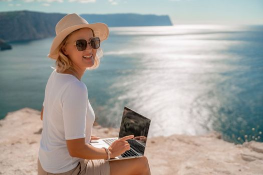 Freelance women sea working on the computer. Good looking middle aged woman typing on a laptop keyboard outdoors with a beautiful sea view. The concept of remote work