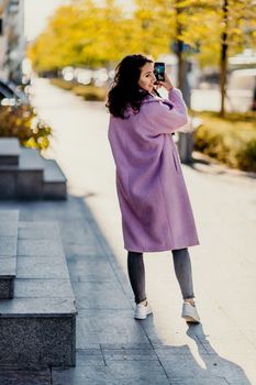 Woman autumn city. A woman in a pink faux fur coat posing on a city street in autumn on a sunny day. Trees with yellow foliage along the street